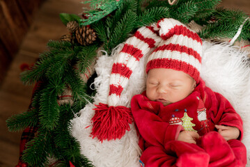 Fototapeta na wymiar A cute little baby in a red suit and a cap is sleeping in a Christmas decoration. Christmas mood. Happy childhood.
