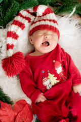 A cute little baby in a red suit and a cap is sleeping in a Christmas decoration. Christmas mood. Happy childhood.