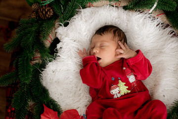 A cute little baby in a red suit is sleeping in a Christmas decoration. Christmas mood. Happy...