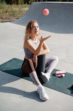 Beautiful sporty woman throwing up ball while sitting at the yoga mat