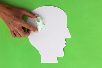 Brain paper cutout with green ribbon on green background with copy space. Mockup for world mental...