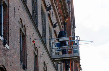 Worker cleaning the window of a building at heigt in lifting cradle. Construction workers at height...