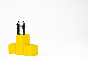 business miniature people shaking hands on yellow podium on white background