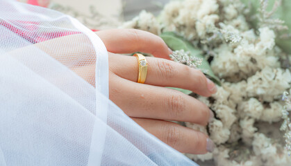 Close up of elegant diamond with golden ring on the female finger and white veil background. Love and wedding concept.