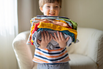 boy holding a stack of clothes. Kids clothing fashion.