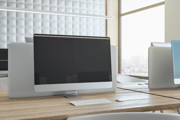 Black blank modern computer monitor screen with place for your logo or text on wooden workspace table in sunlit coworking office with city view. 3D rendering, mock up