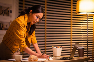Young beautiful woman in yellow shirt work late from home in living room at late night...