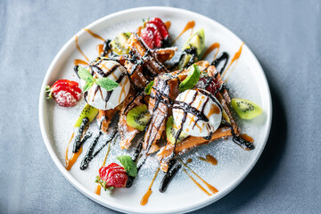 Plate of Belgian waffles with ice cream, caramel and chocolate sauce garnished with fresh berries and mint.