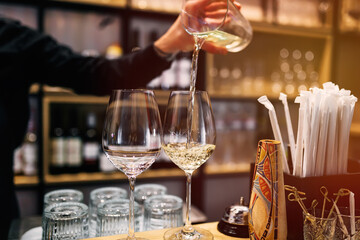 the hand of a waiter pouring white wine into glasses at the bar of an expensive restaurant.