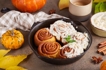 Pumpkin cinnamon rolls. Yeast dough buns in a shape of spiral with sugar and cinnamon filling and cream cheese frosting. Delicious autumn homemade dessert.