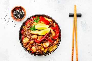 Asian cuisine, stir fry noodles with chicken and vegetables, paprika, zucchini and sesame seeds in bowl. White kitchen table background, top view, space for text