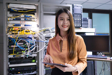 Portrait of young woman wearing glasses using digital tablet standing against server cabinets in...