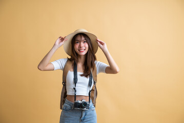 young attractive Asian woman traveler in casual clothes wearing straw hat with backpack and camera isolated on yellow background, Tourist girl having cheerful holiday trip concept
