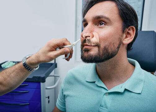 Adult man during rhinoscopy in ENT office. Doctor using nasal speculum or rhinoscope to examine patient's nose area