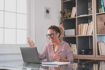 One young woman working at home in the office with laptop and notebook taking notes talking in a video conference. One businesswoman calling communicating.