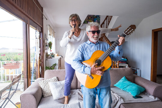 Happy and funny couple of old and mature people having fun and enjoying at home doing a party together singing and dancing playing the guitar indoor. Holiday or event celebrating concept..