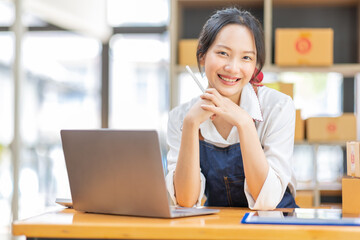 Young Asian SME small business owner working at home office, taking note on purchase orders. Online marketing packaging delivery, startup SME entrepreneur or freelance woman concept