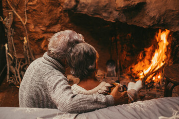Portrait of cute mature senior enjoying Christmas in front of hot fireplace at home feeling cold embracing together and holding their hands. Wearing colored holiday socks in feet..