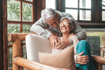 Portrait of couple of happy mature people in love hugging and looking at the camera smiling and having fun at home. Two cute seniors enjoying indoors together.