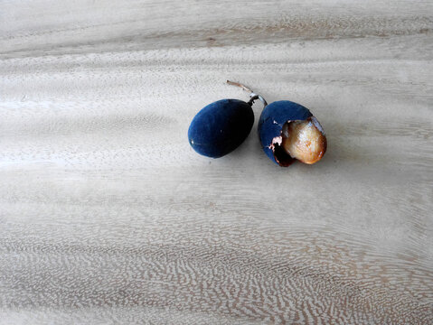 Close up of Black Velvet tamarind plum (Dialium cochinchinense) with shell and half open, on the wooden table, Thai folk name Lookyee, sour and sweet taste when ripe with black peels.