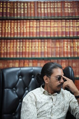 young man with pony sitting on chair wearing sunglasses in libraray