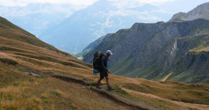Man with a backpack hiking on a trail of the Alps moutains in summer, evocation of outddoors, freedom, trekking