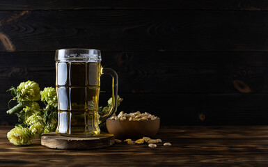 A tall transparent beer glass with facets stands on a wooden stand. Golden beer shimmers in the...