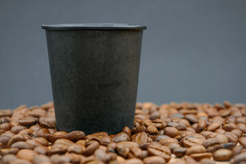 A mug of black coffee stands among coffee beans. Black paper cup. Coffee beans. Coffee cup.
