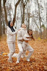 Fototapeta premium Young family playing in autumn forest and throwing a daughter in the air