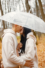 Lovely couple standing in autumn forest and kissing under a transparent umbrella