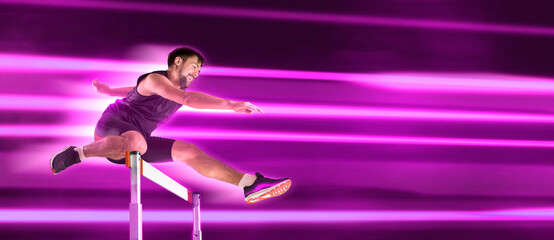 Young male athlete at hurdle race, jumping over the last hurdle