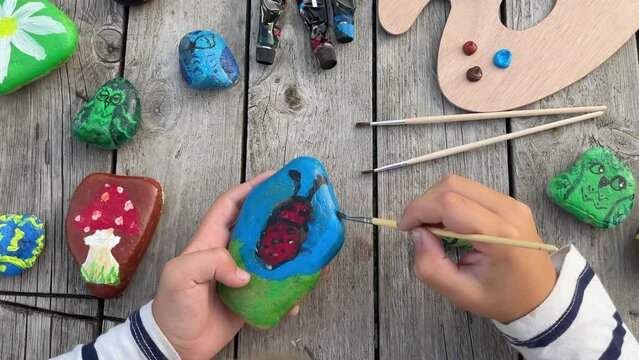 footage of a child's hands drawing a fungus on a stone with acrylic paints. Home hobbies are authentic. Artwork on stones.