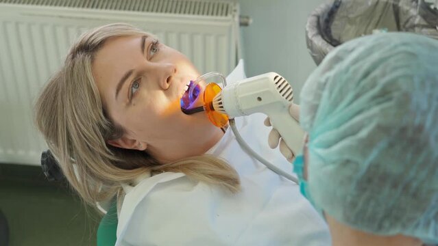 the dentist dries the seal with a polymerization lamp in a woman's mouth
