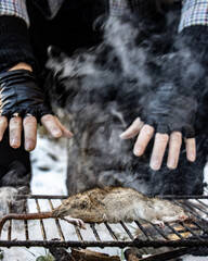 The moving hands of a homeless man over the grill of a rat, close up view.