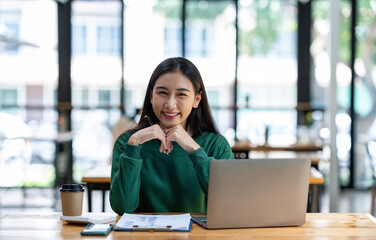 Asian businesswoman working with laptop at her desk in the modern office looking and smiling at the camera