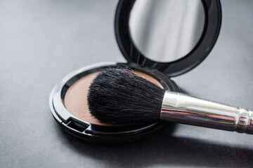 Close-up of a black makeup brush. On the background of an open box with pink powder. Dark, almost...
