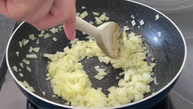SLOW MOTION SHOT - Preparing farofa (Brazilian toasted cassava flour) by toasting in a pan on the electric stove. Onions and garlic are fried in a pan while stirred by a wooden spoon.