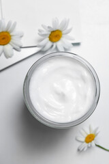 Fototapeta na wymiar Jar of hand cream and chamomiles on white table, flat lay