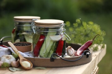 Jars of delicious pickled cucumbers and ingredients on wooden table against blurred background, closeup