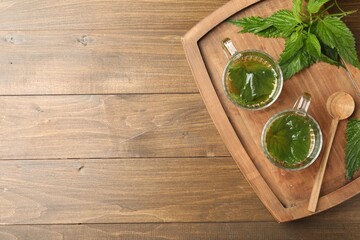 Glass cups of aromatic nettle tea and green leaves on wooden table, top view. Space for text