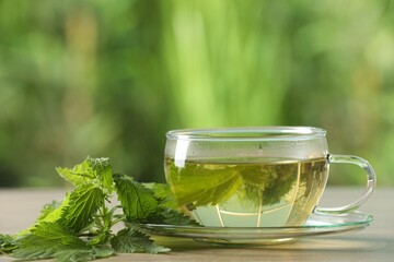Glass cup of aromatic nettle tea and green leaves on table outdoors