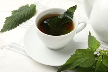 Cup of aromatic nettle tea and green leaves on white wooden table, closeup
