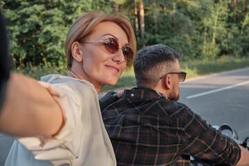 Fototapeta premium Middle age couple riding a motorcycle having fun and taking selfies