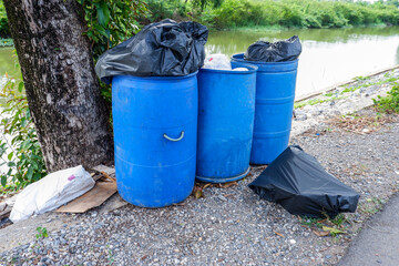 Garbage black bag in blue bin and on the floor with river background