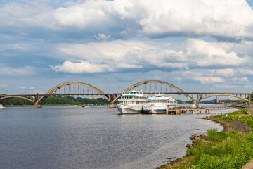 Fototapeta na wymiar RYBINSK, RUSSIA - JULY 9, 2022: Volzhskaya embankment with cruise ships and Rybinsky bridge. Provincial russian city in summer day.