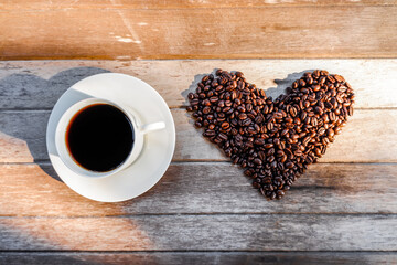 Coffee in white cup with coffee beans in the shape of heart and The morning sunlight  on old wooden background