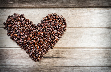 Oasted coffee beans in the shape of heart on a wooden background in the left part of the frame with copy space