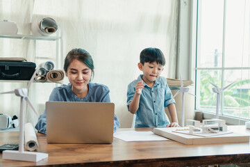 Fototapeta premium A beautiful asian engineer working through the laptop with her son beside, giving the us the working woman and motherhood in one picture.