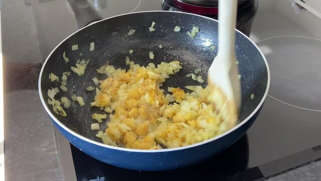 SLOW - Preparing farofa (Brazilian toasted cassava flour) by toasting in a pan on the electric stove. Bananas, onions, and garlic are fried in a pan while adding salt and stirred by a wooden spoon