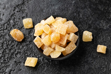 Sweet and spicy candied ginger in black bowl on dark stone background
